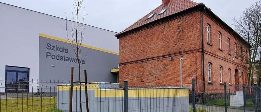 Nowy budynek z szarą elewacją i napisem „Szkoła Podstawowa” obok ceglanego budynku szkoły w Konarzewie